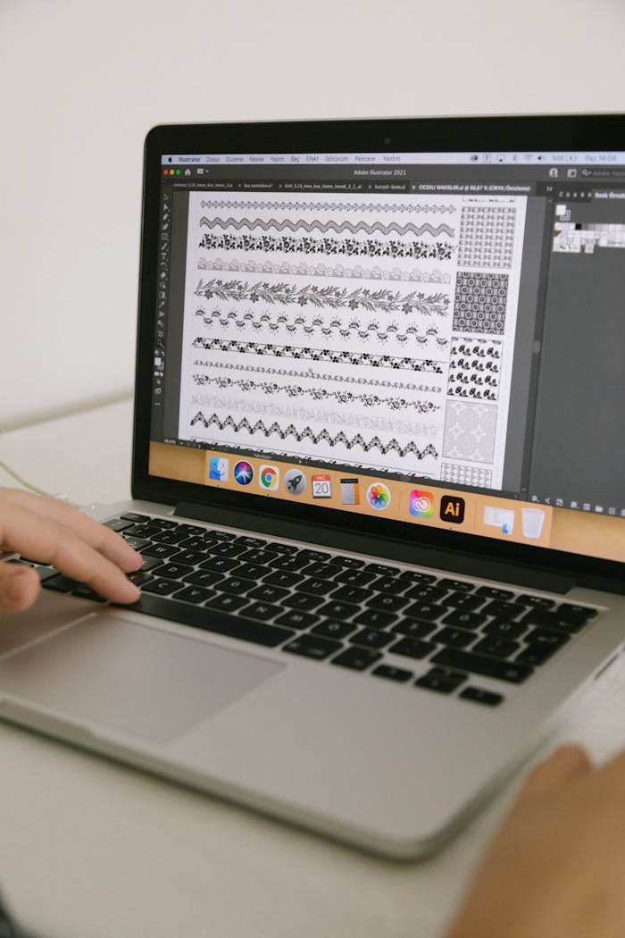 Designer using a laptop to create intricate patterns with graphic software in an indoor setting.
